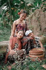 Naklejka na ściany i meble Two girls and boy in traditional clothes in the Bali palm forest.
