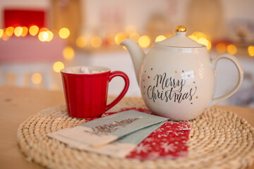 White Ceramic TeaPot with text Merry Christmas and cups with marshmallows on xmas bokeh background