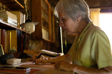 Serious mature woman in glasses writing a letter at home