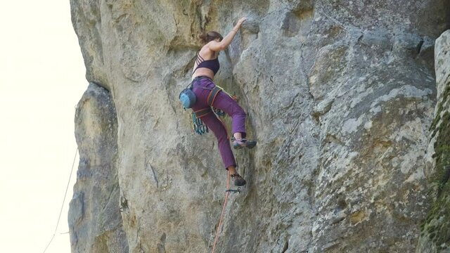 Young woman climber falling down after failed attemp to climb steep wall of rocky mountain. Engaging in extreme sport concept