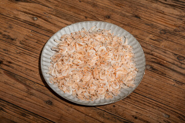 The dried small shrimps in the bowl or plate are on the wooden table