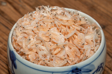 The dried small shrimps in the bowl or plate are on the wooden table