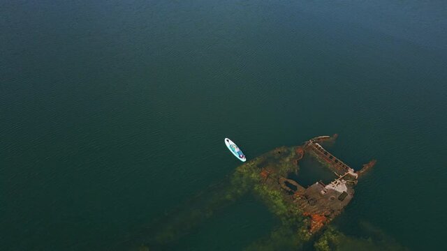 Aerial shot. Young women is having fun. Stand Up Paddling in the sea. SUP. Paddling among debrees of a sunk metal ships