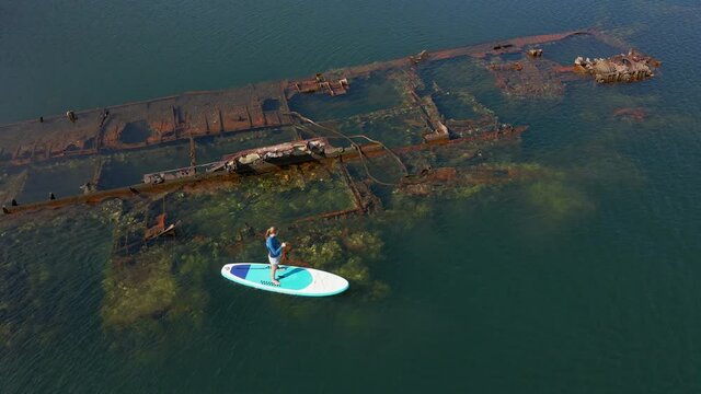 Aerial shot. Young women is having fun. Stand Up Paddling in the sea. SUP. Paddling among debrees of a sunk metal ships