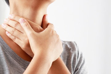 sore throat pain. Closeup of young woman sick holding her inflamed throat using hands to touch the ill neck in blue shirt on gray background. Medical and healthcare concept. Focus red on to show pain.