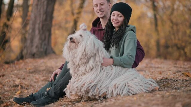 Couple Spending Leisure With Dog. Young happy couple petting their pet while sitting on fallen leaves. Hungarian Shepherd Dog Buli breed in nature.