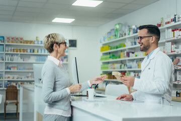 Senior woman customer buying medications at drugstore while talking with a male pharmacist