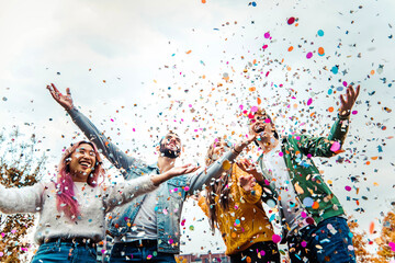 Happy friends celebrating throwing confetti in the air - Young people having outdoor party -...