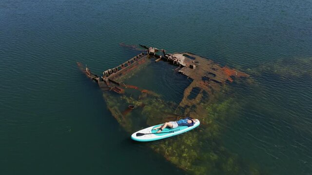 Aerial shot. Young women is having fun. Stand Up Paddling in the sea. SUP. Paddling among debrees of a sunk metal ships