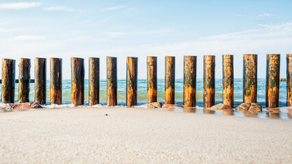 Fototapeta na wymiar Wooden breakwater on the sandy shore, washed by the waves against the background of the sea