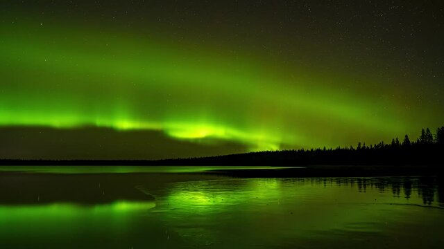 Swilling Aurora reflect in a partially frozen lake. The colors are mostly green and include dramatic action. 
