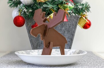 Christmas time, Chocolate Reindeer on a dish in front of a small Christmas tree, facing left