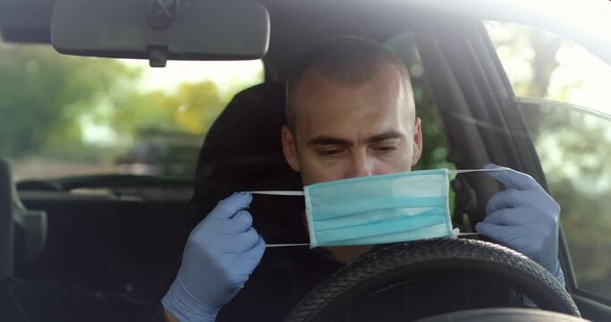 A bald man coughs violently in his car, puts on a face shield to prevent the spread of viruses and bacteria.