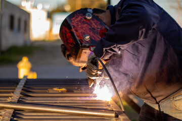 Welder welding a grating wearing a welder helmet with a beautiful welding flash