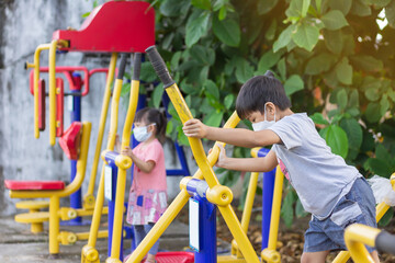 At the park playground. Children are exercise and playing sport machines. Boy and girl wearing face mask.