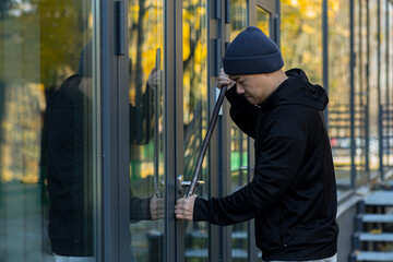 Fototapeta na wymiar Asian man robber tries to break the door lock with a large metal crowbar tool