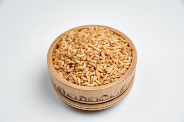 peeled wheat grain in a wooden bowl on a white background