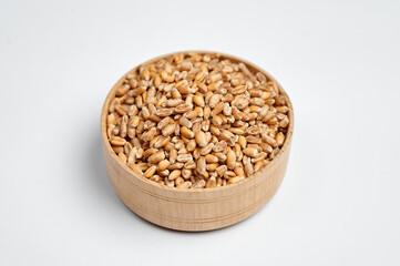 spelled grain in a wooden bowl on a white background