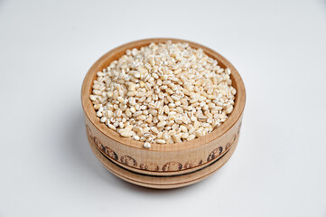 pearl barley grains in a wooden bowl on a white background