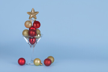 Minimal Christmas party idea. Cocktail glass with flying Christmas bauble balls on blue background.