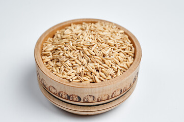 grains of oats in a wooden bowl on a white background
