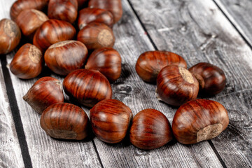 some raw chestnuts, marron (Castanea sativa), a classic autumn fruit, on light colored wooden rustic background with selective focus on foreground.