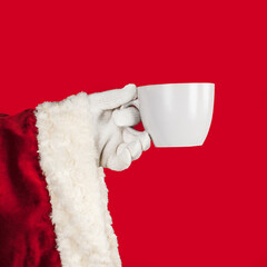 Obraz na płótnie Canvas Santa Claus hand holding a large tea mug on a red background with space for text or numbers