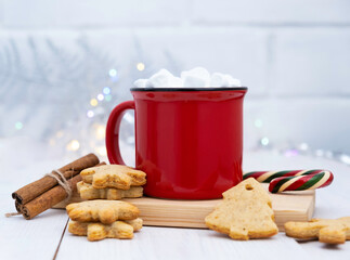 Red mug of cocoa, ginger biscuits, and garlands on a light background.