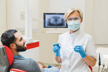 Successful confident caucasian female mature dentist orthodontist stomatologist looking at camera while patient client waiting for tooth teeth filling cleaning