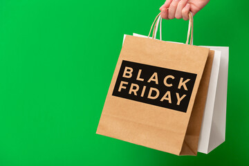 Female hand holding two shopping bags with Black Friday Sale text isolated on green background. White and brown craft blank paper bags in hand. Sale, discount, shopping concept.
