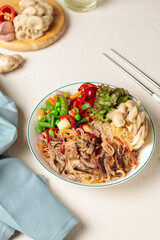 Bowl with funchosa, vegetables, oyster mushrooms and soy meat. Close-up on a light background, vertical