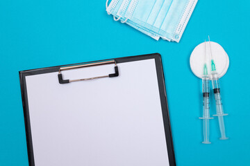 Vaccination, Immunology or Revaccination Concept - Two Medical Syringe Lying on Blue Table in Doctor's Office in a Hospital or Clinic. Black Clipboard with Sheet of Paper - Mock Up with Copy Space