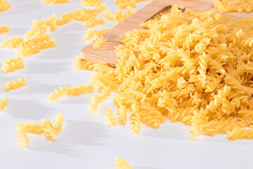 Uncooked Fusilli Pasta Scattered on Wooden Board and White Table. Raw and Dry Macaroni. Fat and Unhealthy Food
