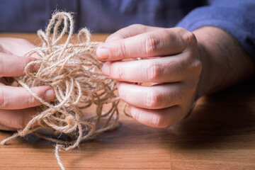 Closeup man try to fix the problem of tangled jute rope - obrazy, fototapety, plakaty
