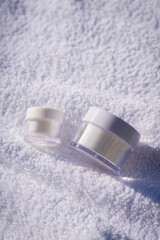 Fototapeta na wymiar Two white jars against the background of a white towel. Skincare products , natural cosmetic. Beauty concept for face body care