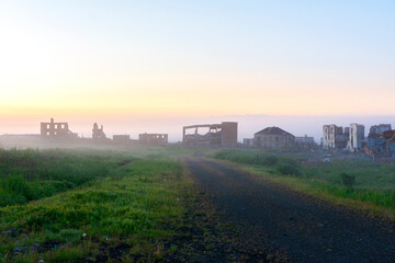 Naklejka premium A real shot of the ghost town in the morning fog. A deserted road leading to the ruins. Halmer-Yu, Russia