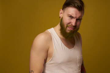 a bearded man with a serious expression in a white t-shirt with tattoos on his arms