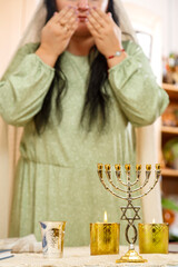 A Jewish woman without a face reads a blessing on the Sabbath candles.