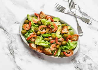 Delicious appetizers salad with shrimp, crispy iceberg, crackers and olives on a light background, top view