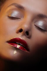Naklejka premium close-up portrait of a beautiful woman with red lipstick and a golden drop on her lips, art makeup, creative