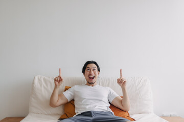 Asian man feels surprised and shocked at empty copy space wall in living room.