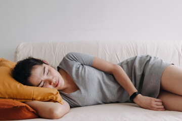 Asian woman in grey dress is sleeping and relaxed on the sofa in the apartment.