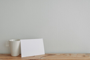 Empty white card mockup lean on a tea cup with white wall background.