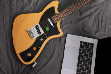 Naklejka premium Electric guitar and laptop laying on a bed