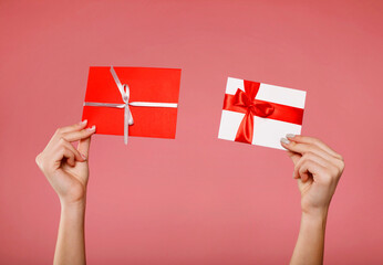 Close up woman's hands hold two different gift certificates isolated on pink background. Holiday...