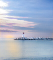 Fototapeta premium white and red lighthouse on a rocky dig by the coast with a sunset calm and blue peaceful turquoise sea