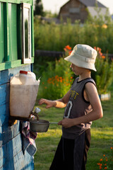 A boy in a headdress, in the summer at the cottage, pours water into the bucket to water the flowers. Banner, cover, flyer, layout design
