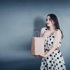 Portrait of a beautiful woman. Dressed in a polka dot dress. Stands with a paper craft bag. Surprise.