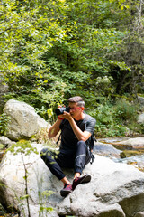Naklejka na ściany i meble Photographer taking pictures on the mountain sitting on a rock