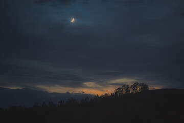 Cloudy sky at sunset with crescent moon.